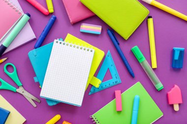 Mor zemin üzerinde farklı kırtasiye malzemesi olan boş bir defter