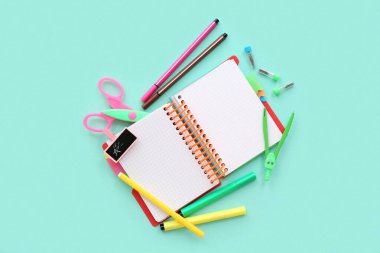 Turkuaz zemin üzerinde farklı kırtasiye malzemesi olan boş bir defter