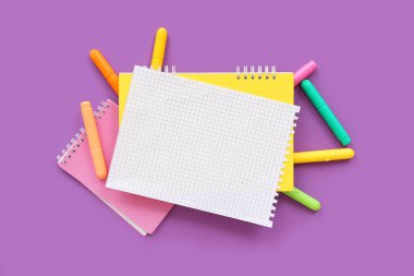 Mor zemin üzerinde farklı kırtasiye malzemesi olan boş bir defter