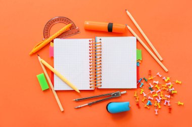 Turuncu zemin üzerinde farklı kırtasiye malzemesi olan boş bir defter