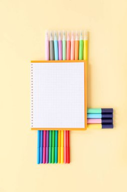 Soluk sarı arkaplanda farklı renkli kalemlere sahip boş bir defter