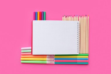 Pembe zemin üzerinde farklı renkli kalemler ve kalemler olan boş bir defter