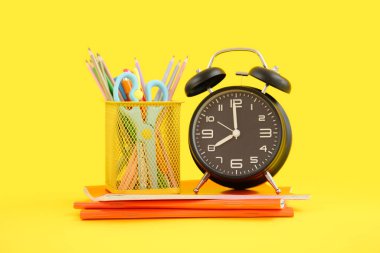 Sarı zemin üzerinde not defterleri ve kırtasiye tutacağı olan alarm saati