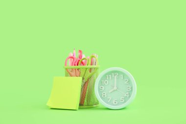 Yeşil arkaplanda farklı kırtasiye malzemesi olan çalar saat