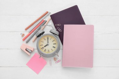 Beyaz ahşap zemin üzerinde farklı kırtasiye malzemesi olan çalar saat