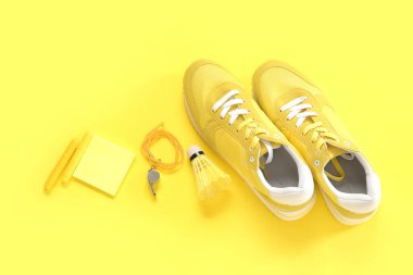 Islıklı spor ayakkabılar, sarı arka planda mekik aleti ve kırtasiye malzemesi.