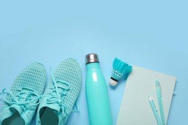 Su şişeli spor ayakkabılar, badminton servis aleti ve mavi arka planda kırtasiye malzemeleri.