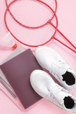 Pembe arka planda badminton servis aleti, raket ve kırtasiye malzemesi olan spor ayakkabıları.