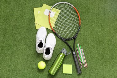 Su şişeli spor ayakkabıları, tenis topu, raket ve arka planda farklı kırtasiye malzemeleri.