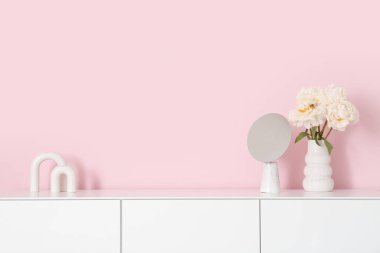 Beyaz şakayık vazosu ve ayna pembe duvarın yanındaki şifoniyerde.