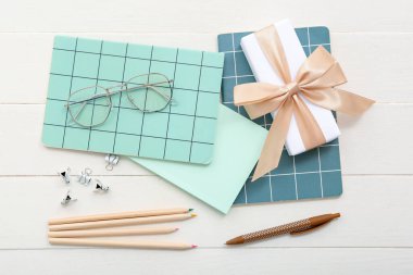 Gözlüklü hediye kutusu ve beyaz ahşap arka planda farklı kırtasiye malzemeleri.