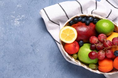 Mavi arka planda farklı taze meyveler olan hasır bir kase.