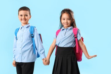 Açık mavi arka planda el ele tutuşan küçük okul çocukları