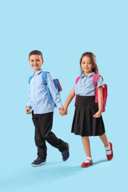 Açık mavi arka planda el ele tutuşan küçük okul çocukları