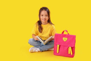 Sarı arka planda kitap ve sırt çantası olan küçük okul kızı.