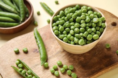 Sarı arka planda taze bezelyeler ve ahşap tabaklar.