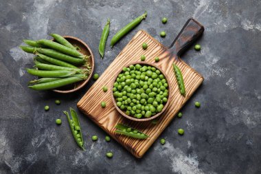 Siyah arka planda taze bezelyeler ve ahşap tabaklar.
