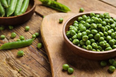 Ahşap zemin üzerinde taze bezelyeler olan kâseler ve yiyecekler.