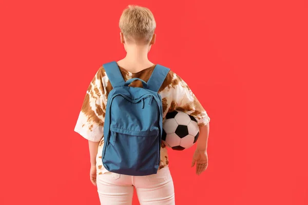 バックパックとサッカーボールを持つ女性学生赤の背景 バックビュー — ストック写真
