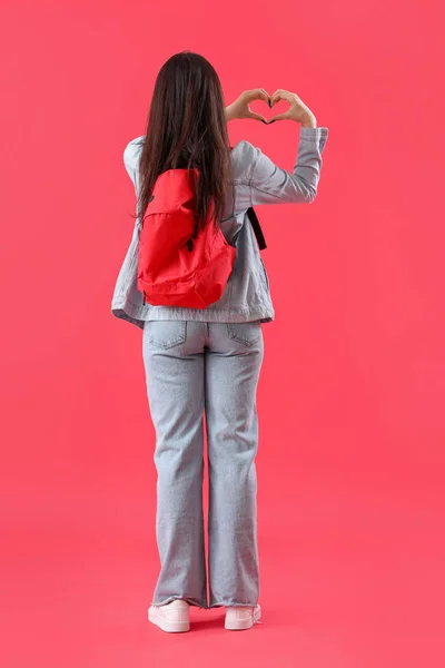 バックパックを持つ女性学生は 赤の背景にハート型を作ります バックビュー — ストック写真