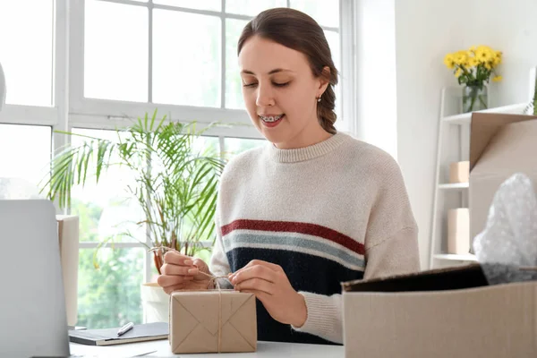 Stock image Young woman packing parcel for client in office