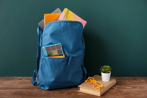 蓝色校服背包 装有笔记本 眼镜和肉质的棕色木制桌子 靠近漆黑的墙壁 — 图库照片