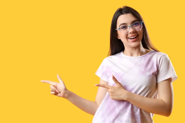 Ładna Młoda Kobieta Nosi Okulary Wskazuje Coś Żółtym Tle — Zdjęcie stockowe