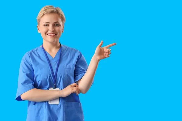 Female Medical Intern Pointing Something Blue Background — стоковое фото