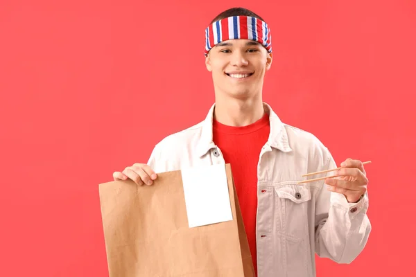 アジア料理と箸付きの紙袋を持っている若い男が赤い背景に — ストック写真