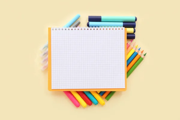 薄い黄色の背景に異なるカラフルなマーカーと鉛筆とブランクノート — ストック写真