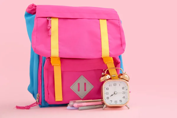 Backpack with alarm clock and stationery on pink background