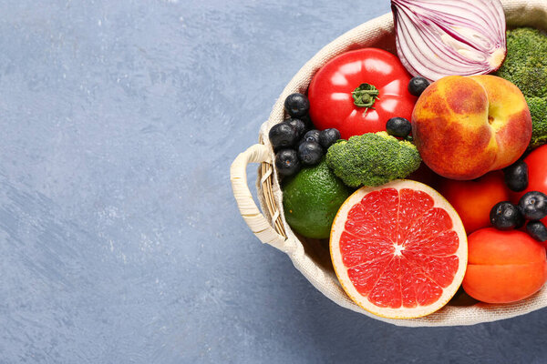 Wicker basket with different fresh fruits and vegetables on blue background, closeup