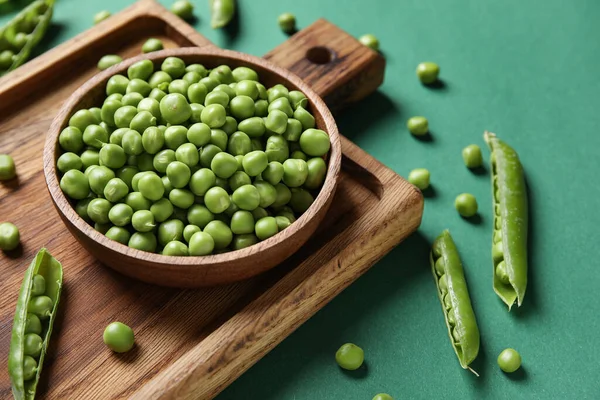 stock image Bowl and wooden board with fresh green peas on color background