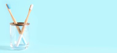Açık mavi arkaplanda bambu diş fırçaları ve metin için yeri olan cam tutucu