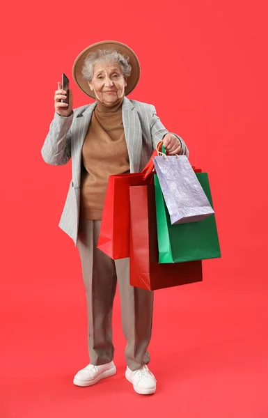 Mujer Mayor Con Teléfono Móvil Bolsas Compras Sobre Fondo Rojo — Foto de Stock