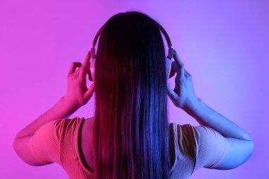 Kulaklıklı genç bir kadın arka planda müzik dinliyor.