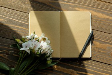 Boş bir defter, kalem ve ahşap arka planda güzel alstromerya çiçekleri.