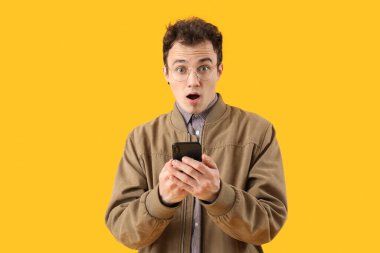 Sarı arka planda akıllı telefonlu şok olmuş genç bir adam.