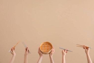 Ellerinde farklı yemek çubukları ve kahverengi arka planda bambu buharı var.