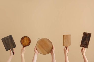 Kadın ve erkek elleri kahverengi arka planda farklı kesme tahtaları tutuyor.