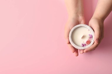 Pembe arka planda çiçekli mum tutan kadın eller.