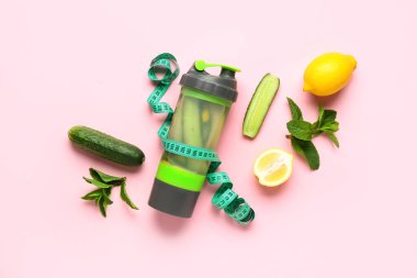 Salatalıklı bir şişe limonata ve pembe arka planda mezura.