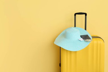 Hasır şapkalı bavul, pasaport, bilet ve sarı arka planda para. Seyahat kavramı