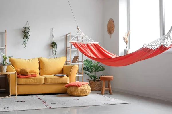 Interior of stylish living room with red hammock, yellow sofa and coffee table