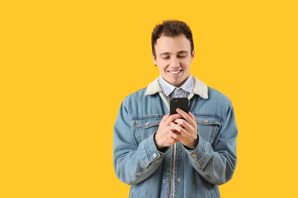 黄色の背景をしたスマートフォンを持つ若い男 — ストック写真
