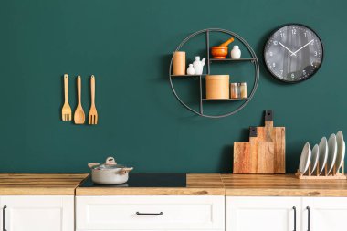 Mutfak tezgahında yeşil duvarın yanında elektrikli ocak var.