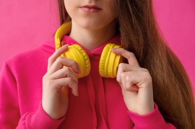 Young woman in headphones listening to music on pink background