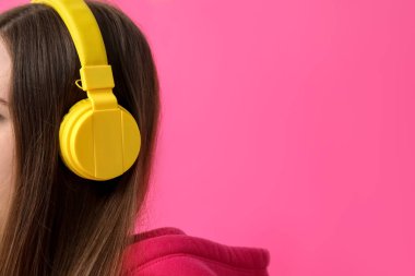 Young woman in headphones listening to music on pink background