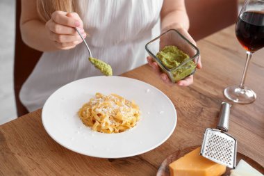 Genç kadın mutfaktaki lezzetli makarnaya pesto ekliyor, yakın plan.