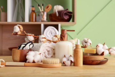 Kozmetik ürünler, banyo malzemeleri ve pamuk dalı renkli duvarın yanındaki ahşap masada.